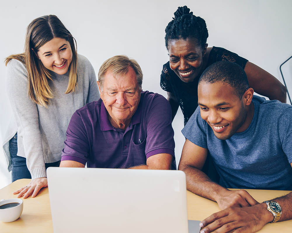 4 people smiling in front of a laptop